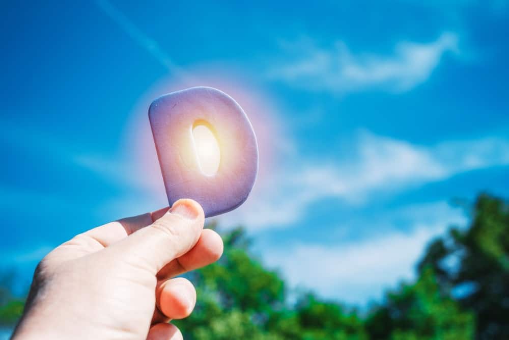 Hand holding a letter D over the sun to highlight the benefits of Sunlight for Vitamin D absorption