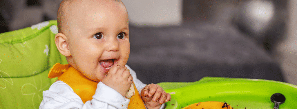 Baby boy sat in a high chair eating